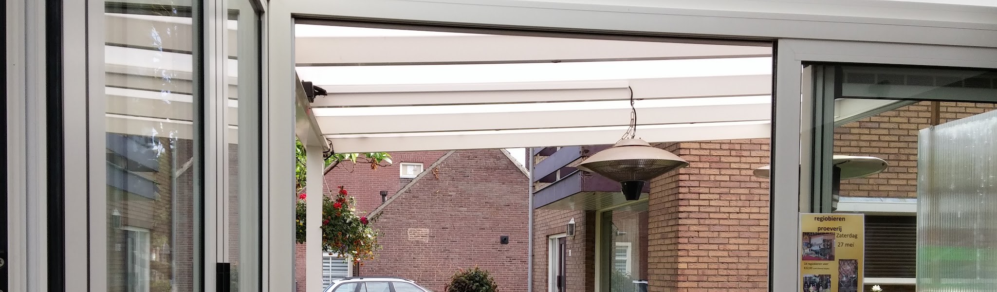 Het overdekte terras aan de zijkant, met terrasverwarmer en hanging baskets